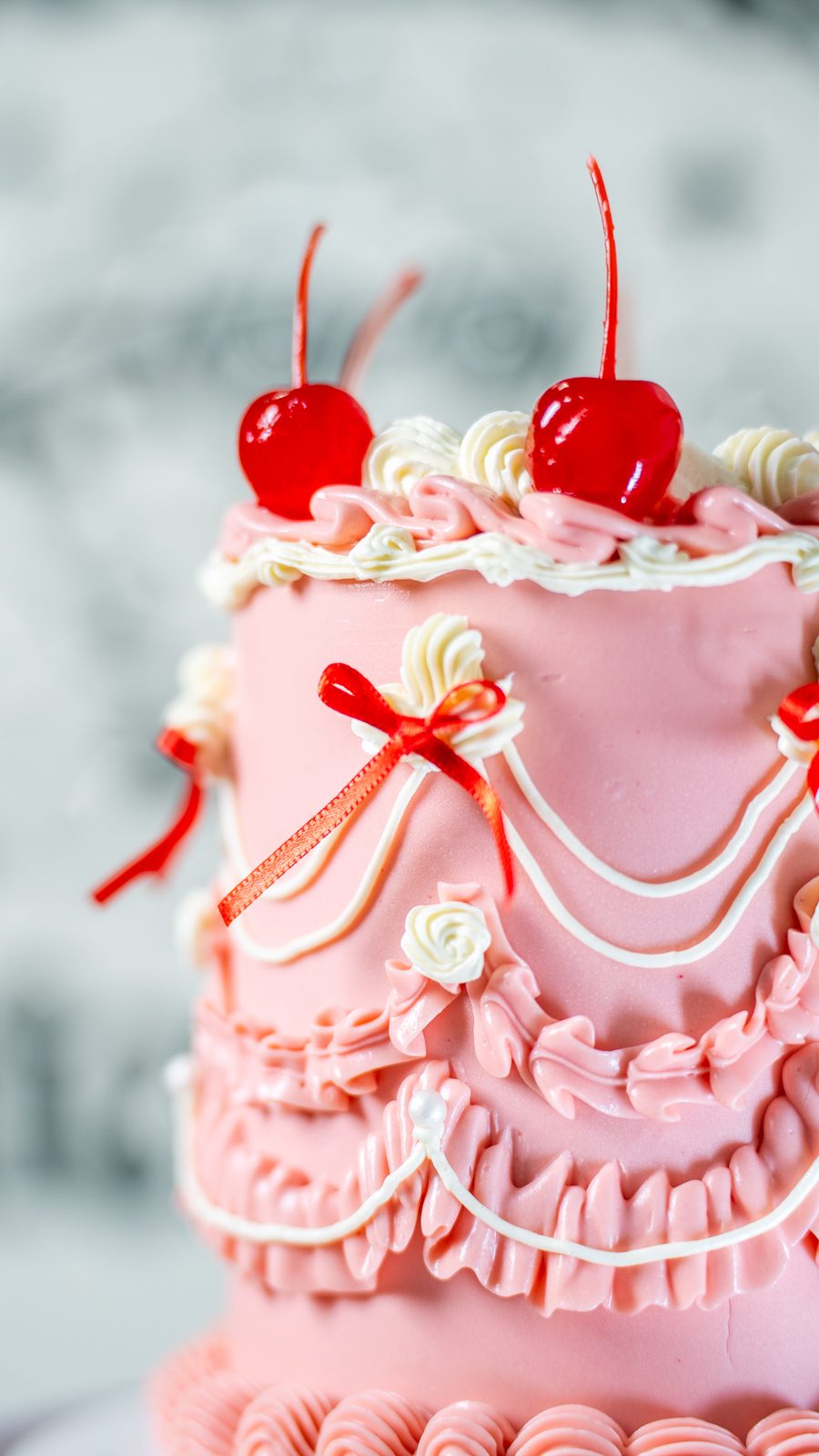Detalhe de um bolo rosa da Gaia: babados de buttercream, pérolas, lacinhos vermelhos e cerejas no topo.